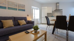 A modern living room with a sofa, a coffee table with a remote control and a plant, and a dining area with chairs and a table. - SAIL Family Home by Cadiz4Rentals (Cádiz)