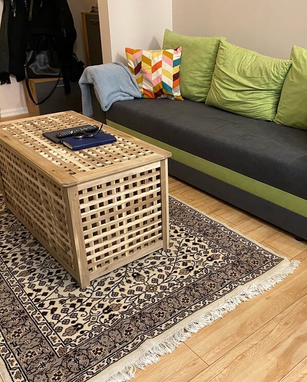 A living room with a wooden coffee table, a patterned rug, a sofa with green cushions, and a colorful pillow. - Brand new Apartment in center of Riga on Avotu street (Riga)