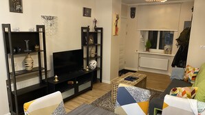 Un salon avec un téléviseur, des étagères ornées d’objets décoratifs, un canapé et une table à manger.