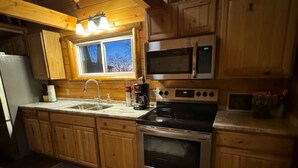A kitchen with wooden cabinets, a stainless steel stove, a microwave, and a sink. - The Cozy Cabin near Geneva on the Lake and Wineries! (Ashtabula)