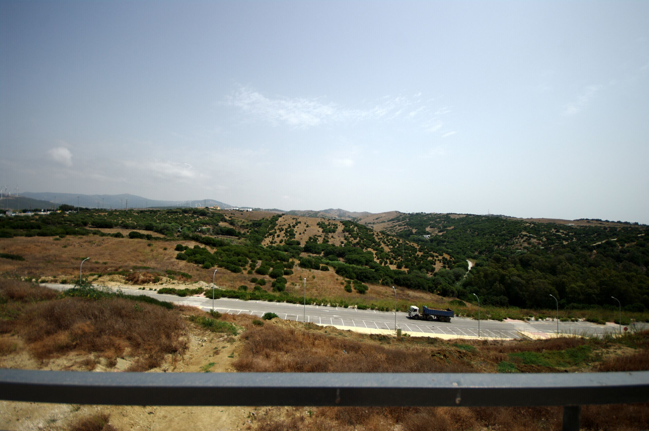 A highway with a truck passing by, surrounded by hilly terrain and sparse vegetation.