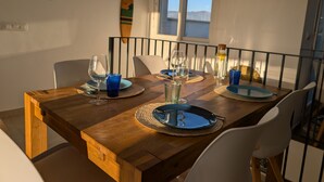 A dining table set with plates, glasses, and cutlery, with a surfboard and a bottle on the wall behind. - 250 - Casa Birgit (Tarifa)