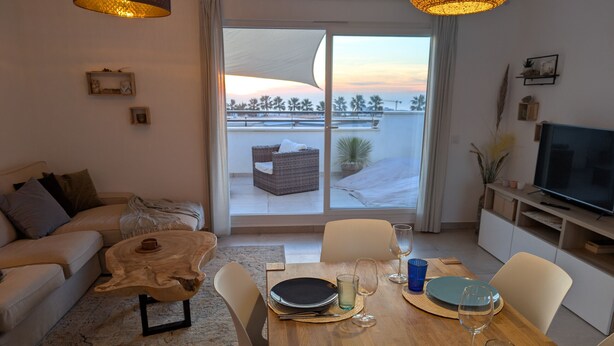A modern living room with a sofa, coffee table, dining table set with plates and glasses, and a TV on a stand. - 250 - Casa Birgit (Tarifa)