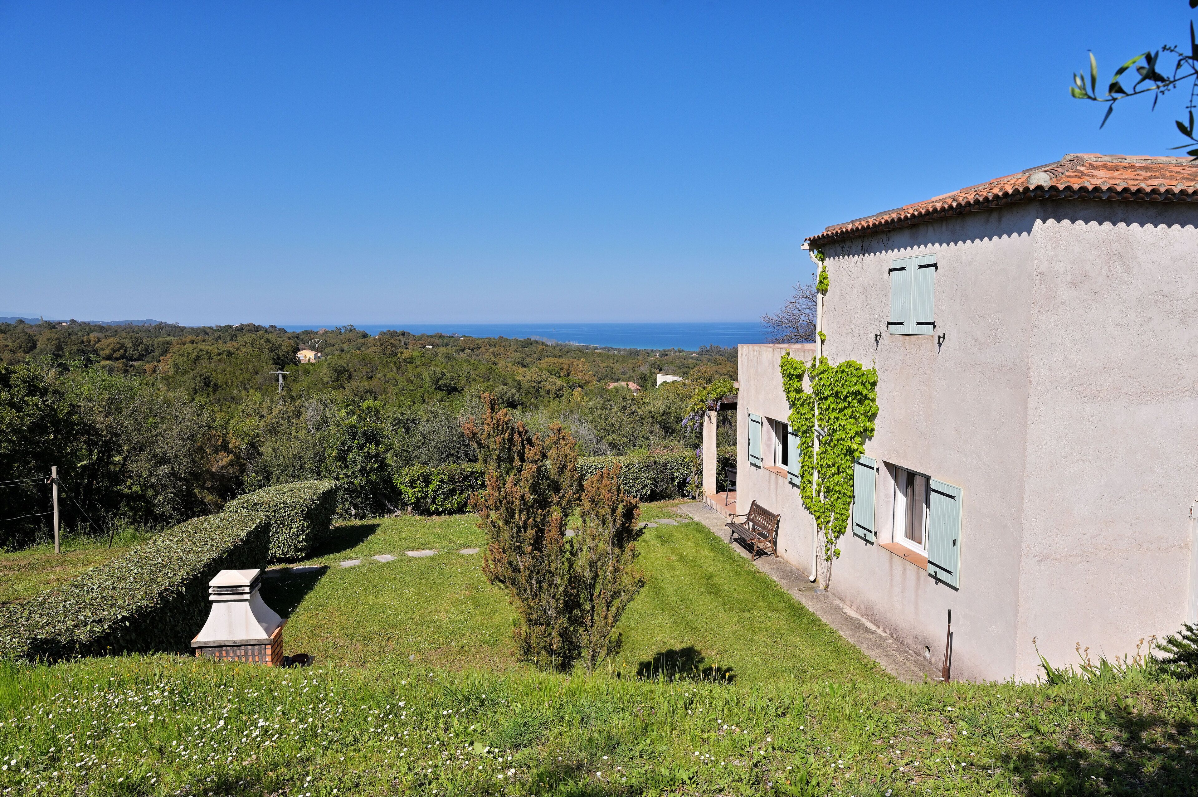 A building with a tiled roof, a bench, and a clear view of the sea.