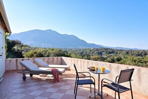 A terrace with a table and chairs, a lounge chair, and a view of a mountain range. - Punta della Guardia Estate, Villa with sea view in a nature reserve, beaches 1.5 Km away (Cervione)
