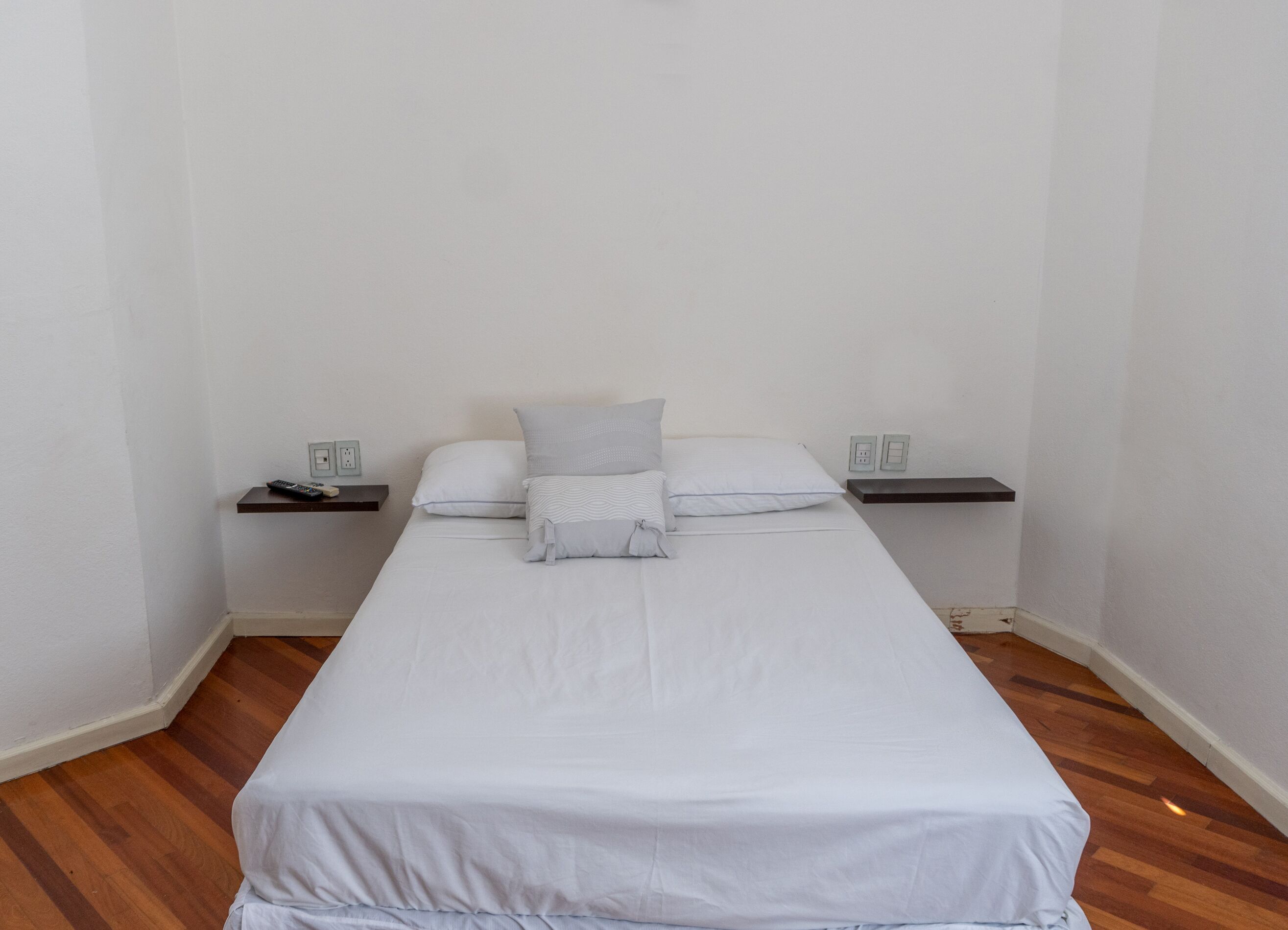 Un dormitorio sencillo y limpio con una cama individual, dos mesitas de noche y suelo de madera.