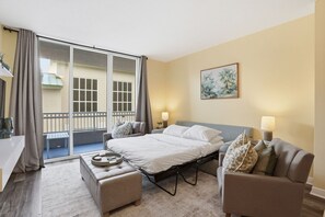 Ein Hotelzimmer mit Bett, zwei Nachttischen, einem Sofa, einem kleinen Tisch mit Tablett und einem Balkon mit Aussicht.
