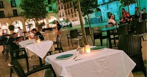 An outdoor dining area with tables set for two, surrounded by trees and a historic building in the background. - Beautiful apartment in the heart of Alicante (Alacant)