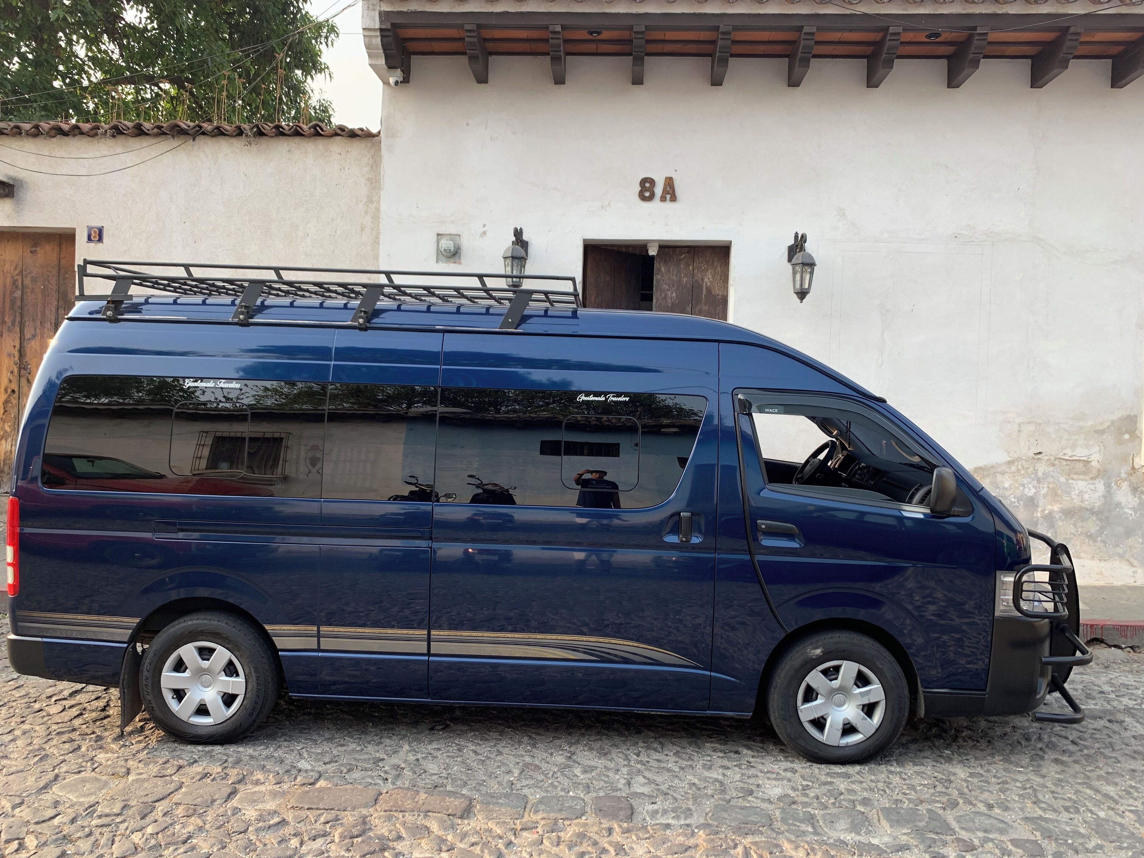 A blue van parked in front of a building with a white facade and a number '8A' sign.