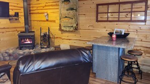 A cozy cabin interior with a fireplace, wooden walls, a stone fireplace surround, a leather couch, and a rustic bar area. - River Ridge Cottage (Spooner)