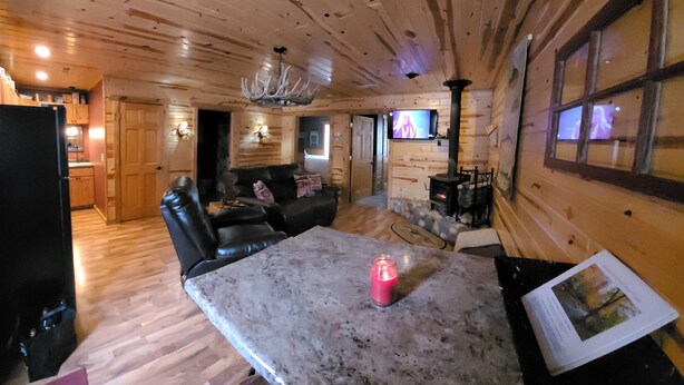 A log cabin interior with a living area, kitchen, and a stone fireplace. - River Ridge Cottage (Spooner)