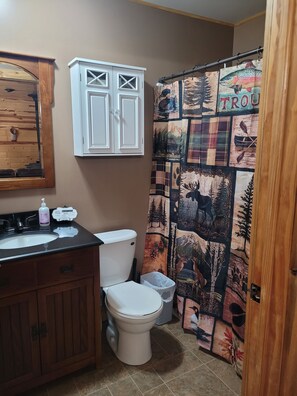 Un baño con un mueble de madera, un inodoro, un lavamanos y una cortina de ducha con motivos forestales.