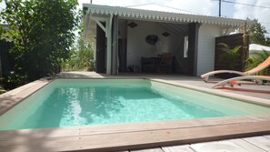 A rectangular pool with a wooden deck surrounding it, a covered outdoor seating area, and a building with a white exterior and a covered porch. - Courbaril villas, Two bungalows with private pools and sea view (st louis)