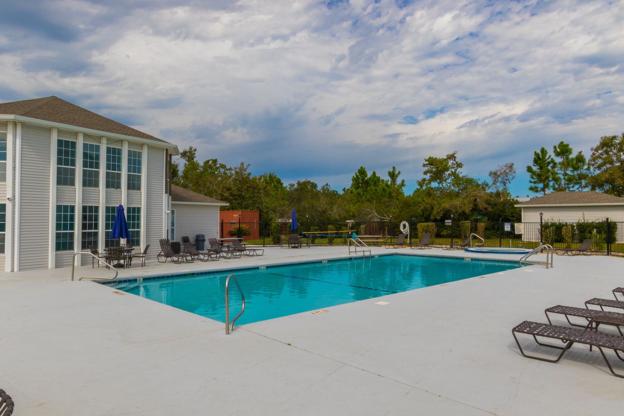 A rectangular swimming pool with a metal ladder, surrounded by lounge chairs and umbrellas.