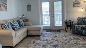 A living room with a beige sectional sofa, a patterned rug, a ceiling fan, and a view through glass doors to the outside. - LOCATION**LOCATION**LOCATION (Gulf Shores)