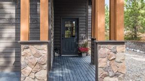 Una casa de madera con entrada de piedra, una puerta negra y un pequeño jardín con flores rojas.