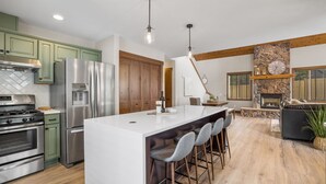 Una cocina moderna con una isla central, taburetes de bar, una chimenea de piedra y vigas de madera en el techo.