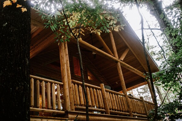 Une cabane en bois dotée d’un balcon et offrant une vue sur la forêt environnante.