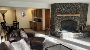 A living room with a stone fireplace, leather sofa, and a dining area with wooden cabinets.