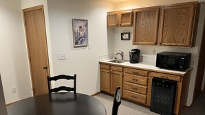 A compact kitchen with wooden cabinets, a microwave, a coffee maker, and a dishwasher.