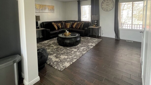 A spacious living room with a dark wood floor, a black leather sofa, a round coffee table, and a patterned rug.