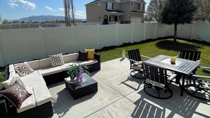 A patio with a sofa set, a dining table, and chairs. There is a white fence surrounding the area.