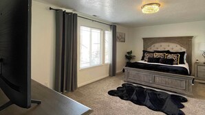 A bedroom with a bed, a TV on a stand, a carpeted floor, and a chandelier.