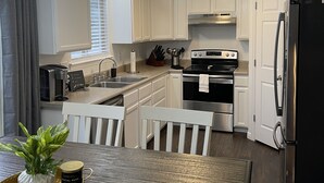 A modern kitchen with white cabinetry, stainless steel appliances, and a dining area with a wooden table and chairs.