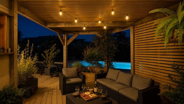 An outdoor patio with wicker furniture, a pool in the background, and string lights.