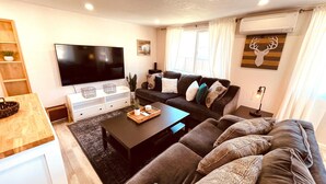A modern living room with a flat-screen TV, a dark sofa set, a coffee table, and a small side table with a lamp. - Westside ^Cottage^ (Redding)