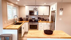 A modern kitchen with white cabinets, stainless steel appliances, a wooden countertop, and a hanging light fixture. - Westside ^Cottage^ (Redding)
