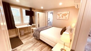 A bedroom with a bed, bedside table, lamp, desk, chair, and a TV. - Westside ^Cottage^ (Redding)
