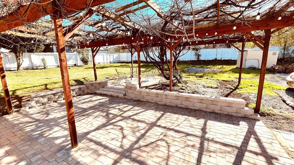 A covered patio area with a brick floor, wooden pergola, and string lights. - Westside ^Cottage^ (Redding)