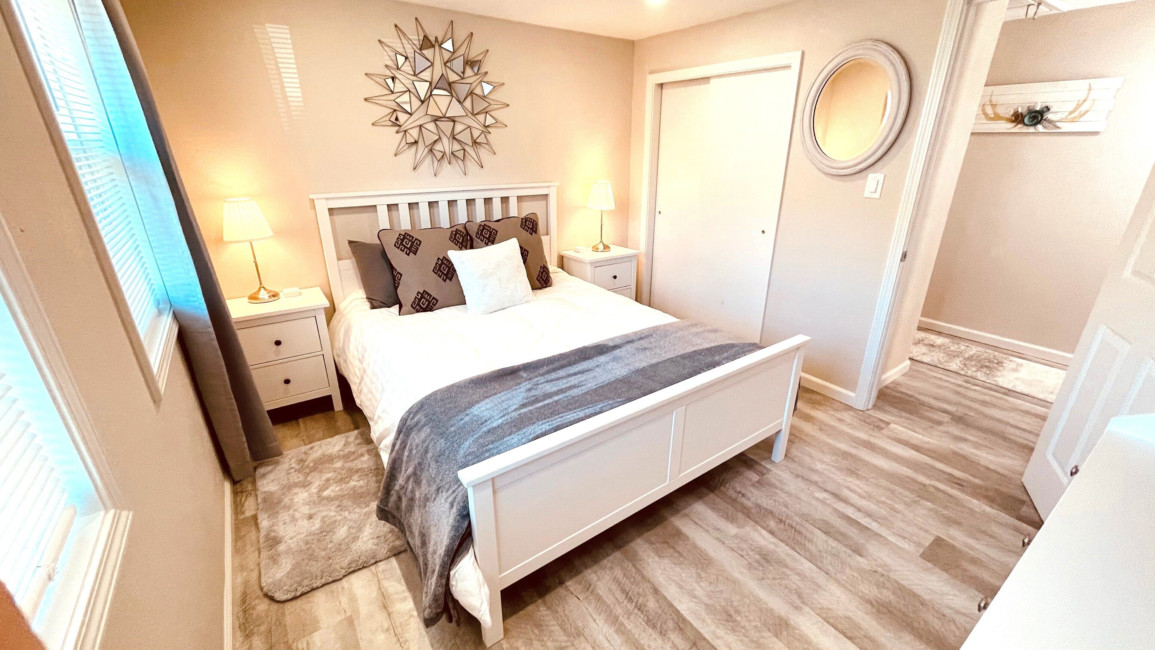 Une chambre à coucher comprenant un lit, des tables de chevet, une lampe, un miroir et un élément décoratif mural.
