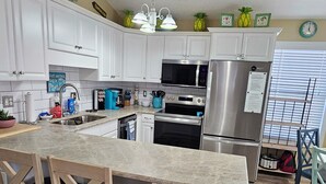 A modern kitchen with white cabinets, a granite countertop, stainless steel appliances, and a wooden dining area.
