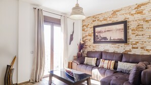 A living room with a brown leather sofa, a glass coffee table, and a brick-patterned wall with a framed picture.