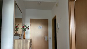 Un pasillo con puerta de madera, un espejo y un jarrón con flores.