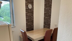 Un comedor con una mesa de madera y cuatro sillas, un reloj de pared y un ventanal con vistas a zonas verdes.