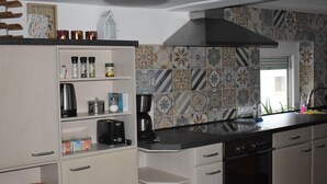 A kitchen with white cabinets, a black stove, and a tiled backsplash. - Vacation home Zum Unneschmitz, near the Rhine/Moselle, (Udenhausen)