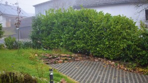 A garden pathway with a metal grate, surrounded by a hedge and rocks. - Vacation home Zum Unneschmitz, near the Rhine/Moselle, (Udenhausen)