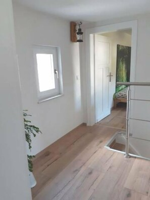 A hallway with wooden flooring, a white door, and a small window.