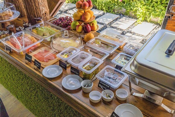 A buffet with various food options including meats, cheeses, fruits, and eggs.
