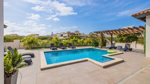 A swimming pool with lounge chairs, a pergola, and a view of surrounding buildings. - NEW 6BR Villa w/ Pool across street @ PalmBeach (Noord)