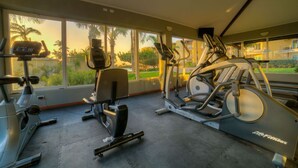 Et fitnesscenter med løbebånd, træningsbænke og et stort vindue med udsigt til palmer.