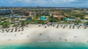 Oversigtsbillede af et resort med flere bygninger, en stor sandstrand og et poolområde.