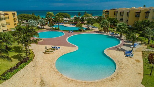 Et resort med en stor, buet swimmingpool omgivet af palmer og liggestole.