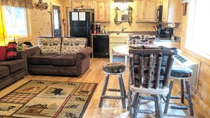 A cozy cabin-style kitchen with wooden cabinets, a refrigerator, a dining table with rustic chairs, and a patterned rug on the floor.