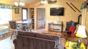 A cozy cabin interior with a wooden ceiling, a television mounted on the wall, a fireplace, and skis leaning against the wall.