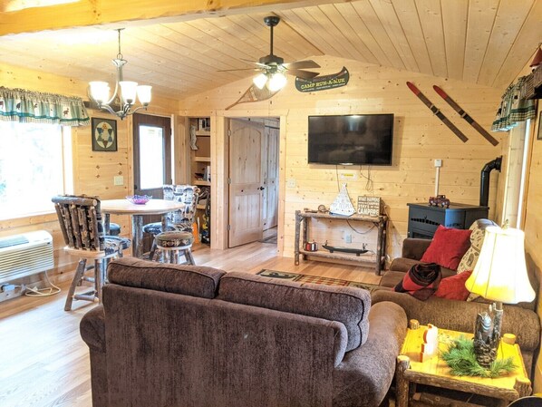 A cozy cabin interior with a wooden ceiling, a television mounted on the wall, a fireplace, and skis leaning against the wall. - Summer Fun in Necedah WI at Lazy Moose Lodge! (Necedah)