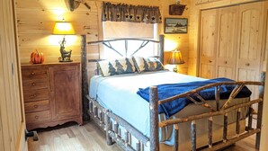 A rustic wooden bedroom with a bed, a nightstand, a dresser, and a lamp.